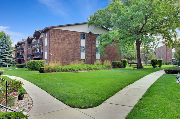 Front elevation view of a brick apartment building with balconies and surrounding greenery.