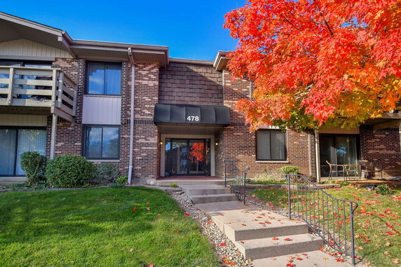 Front view of a multi-story brick apartment building with an entrance and surrounding red foliage.