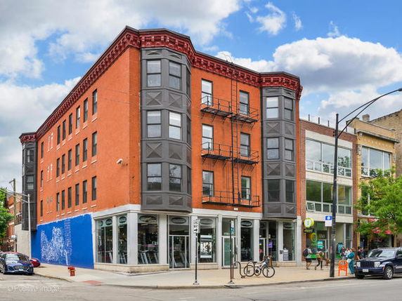 Front view of a three-story commercial building with large windows and fire escape ladders.