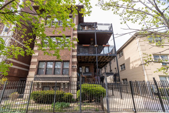 Front view of a multi-story brick apartment building with balconies and a metal fence.