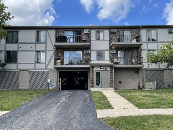 Front view of a three-story apartment building with balconies and a driveway.