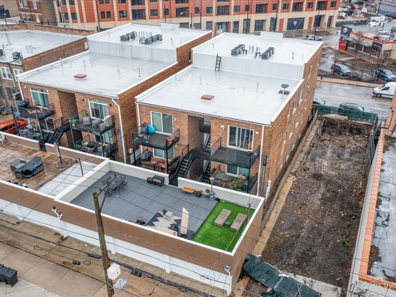 Aerial view of brick buildings with flat rooftops featuring HVAC units and a rooftop patio with seating.