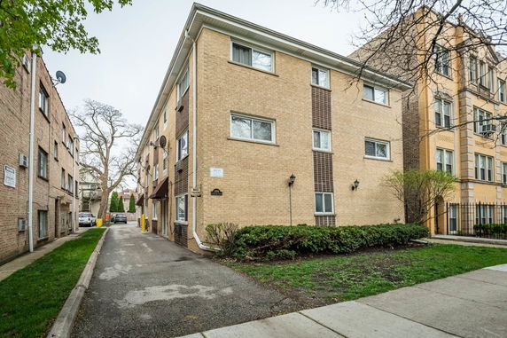 Front view of a multi-story apartment building with a partial brick facade and several windows.