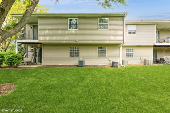 Rear view of a two-story residential building with a small patio and air conditioning units.