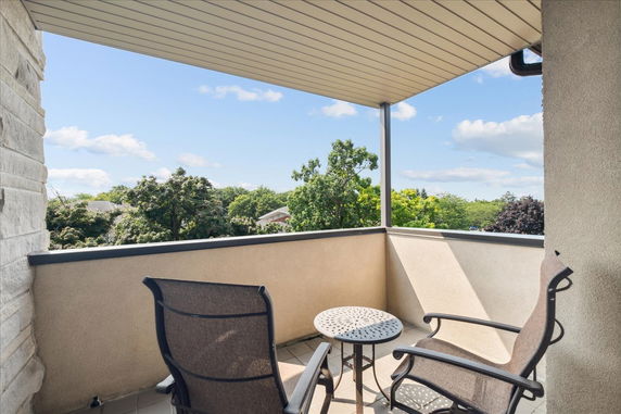 Balcony with chairs and a table overlooking trees.