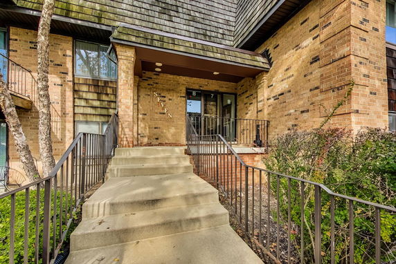 Front view of a brick building entrance with stairs and railing.