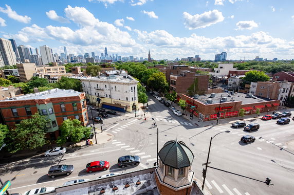 Cityscape view featuring streets, mixed-use buildings, and a distant skyline under a partly cloudy sky.