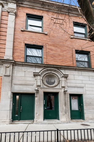 Front view of a multi-story brick building with ornate stone detailing and dark green doors.