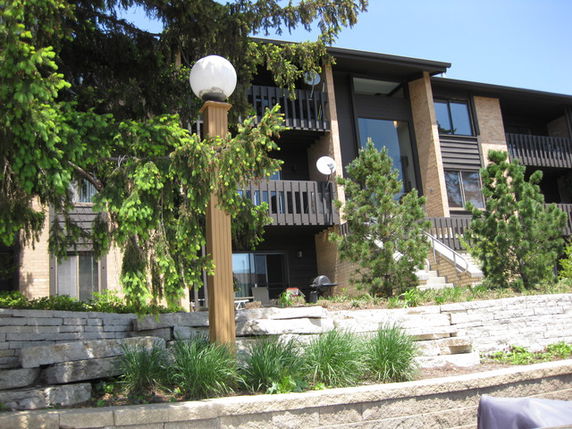 Front view of a multi-story building with balconies and a landscaped area, including a streetlamp.