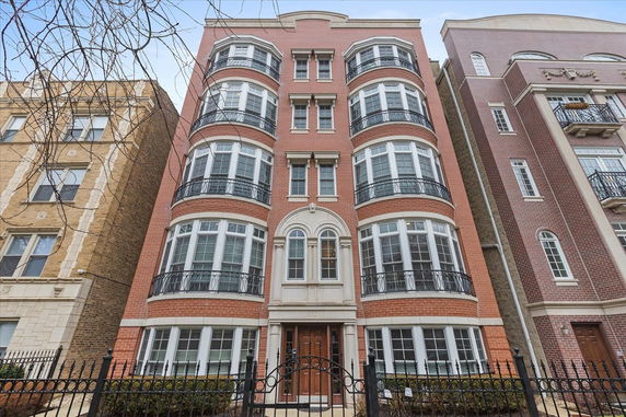 Front view of a multi-story brick residential building with large windows and wrought iron balconies.