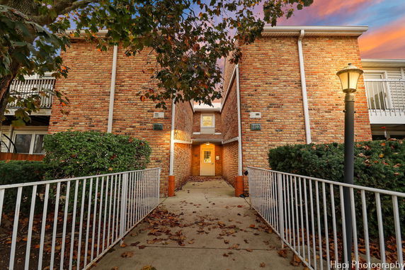Front view of a brick apartment building with a central entrance and white railings.