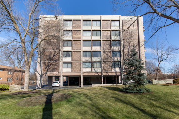 Front view of a multi-story apartment building with parking space underneath.