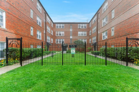 Front view of a multi-story brick building with a fenced courtyard.