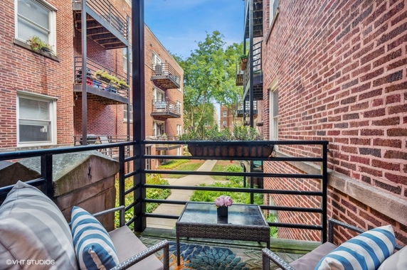 View of brick apartment buildings from a small balcony with seating and a table.