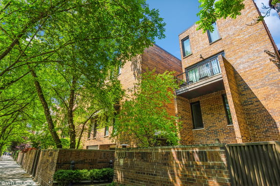 Front view of a multi-story brick building with a balcony and surrounding trees.