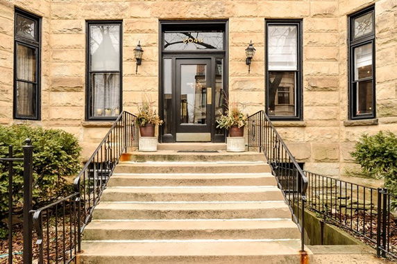 Front view of a building with stone exterior, steps leading to a black door, and surrounding windows.