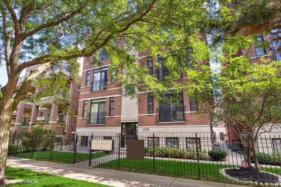 Front view of a multi-story brick residential building with large windows and a gated entrance.