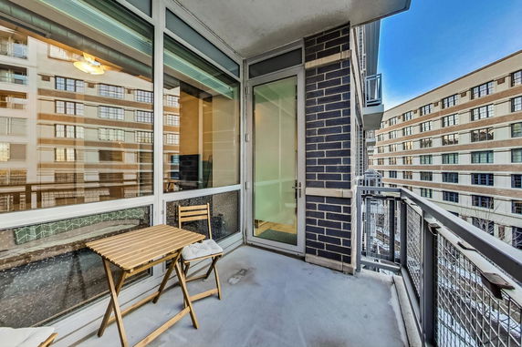 Outdoor balcony view of a residential building with glass windows and a small seating area.