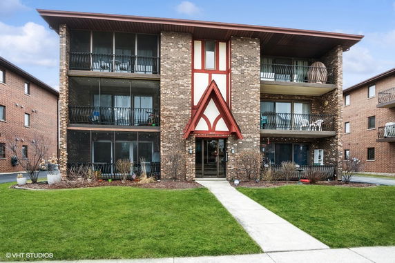 Front view of a three-story brick apartment building with balconies and a central entrance.