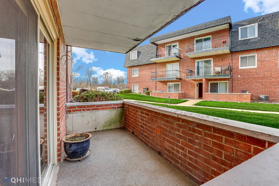 View from a balcony overlooking a brick apartment building with balconies and a landscaped area.