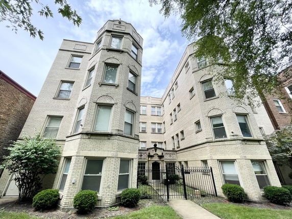 Front view of a multi-story apartment building with pale brick exterior and decorative window arches.