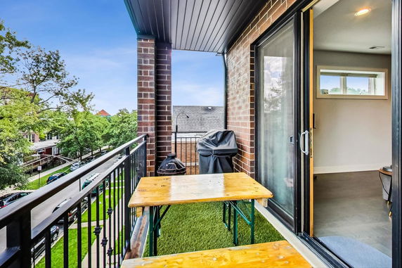 Balcony with a wooden table and chairs, overlooking trees and buildings.