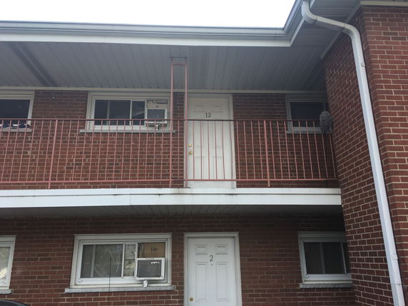 Front view of a two-story brick building with doors numbered 2 and 12, featuring a metal railing and windows with AC units.