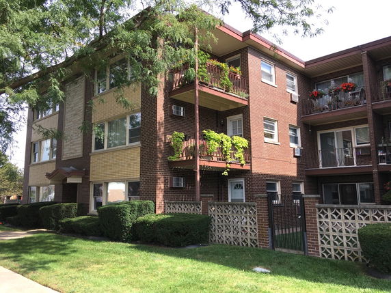 Front view of a three-story brick apartment building with balconies and a small gated entrance.