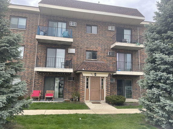 Front view of a three-story brick apartment building with balconies.