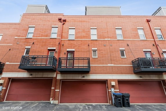 Front view of a brick multi-story building with balconies and garage doors on the ground level.