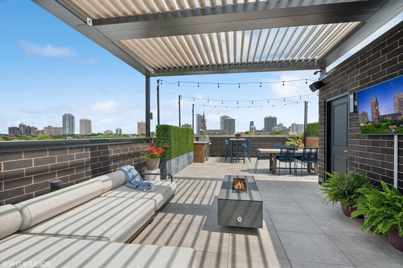 Rooftop patio with seating area, fire pit, and view of city skyline.