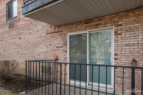 Exterior view of a building with a brick facade and a sliding glass door leading to a small balcony with a metal railing.