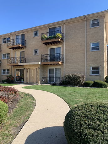 Front view of a three-story building with balconies and a pathway leading to the entrance.