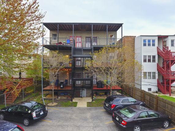 Rear view of a multi-story apartment building with balconies and an open parking area.