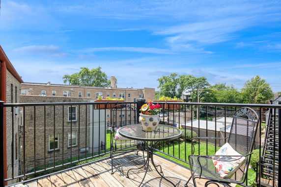 View from a balcony with outdoor furniture and planters overlooking nearby buildings and greenery.