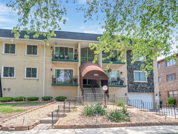 Front view of a two-story residential building with balconies and an entrance awning.