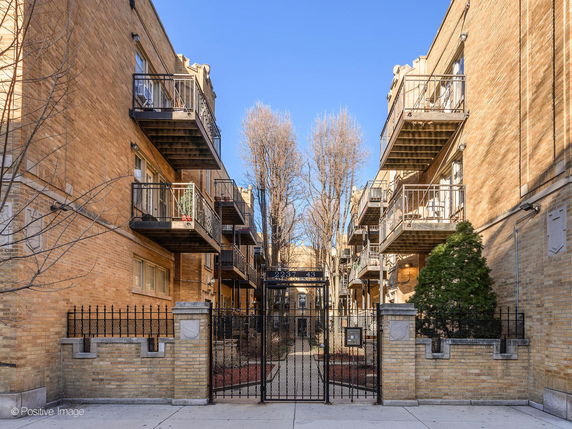 Front view of a brick apartment building with balconies and a metal gate entrance.