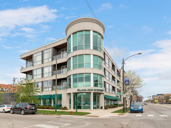 Front view of a modern multi-story building on a city corner with large glass windows and rounded design.