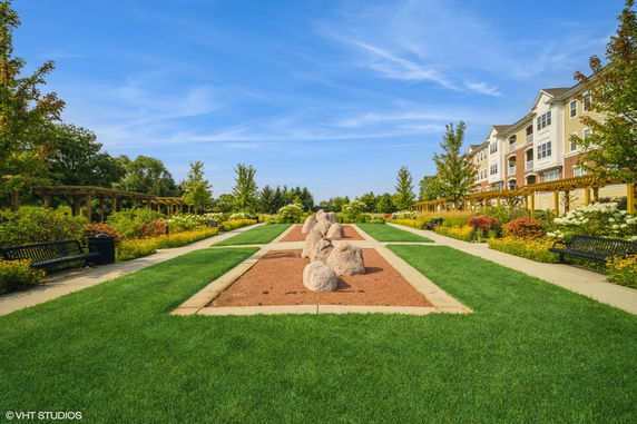 View of a landscaped garden with walking paths and seating in front of a multi-story building.