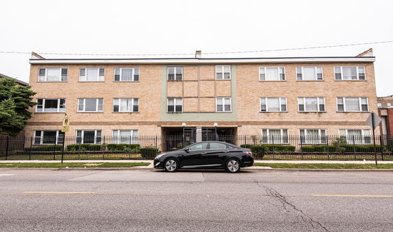 Front view of a three-story brick apartment building with a car parked in front.