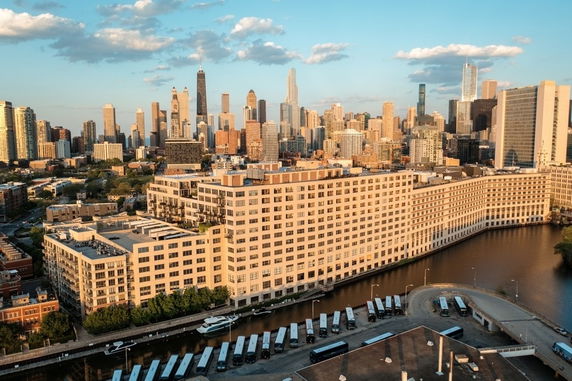 Aerial view of a cityscape with a large waterfront building and numerous skyscrapers in the background.