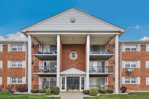 Front view of a three-story brick apartment building with balconies and white columns.
