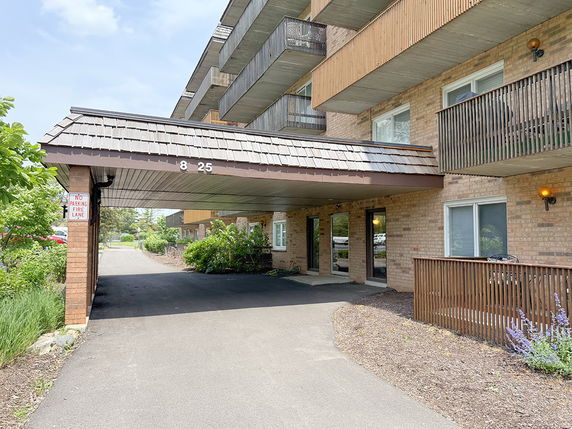 Front view of a multi-story apartment building entrance with balconies and a covered driveway.
