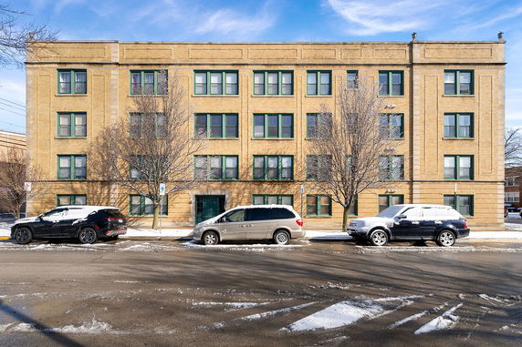 Front view of a four-story brick building with multiple windows and parked cars in front.