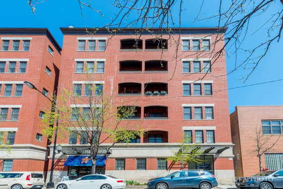 Front view of a multi-story brick building with balconies and blue sky.