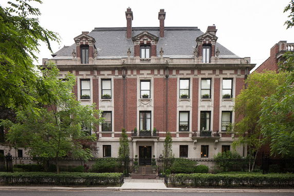 Front view of a large multi-story brick house with ornate windows and chimneys.