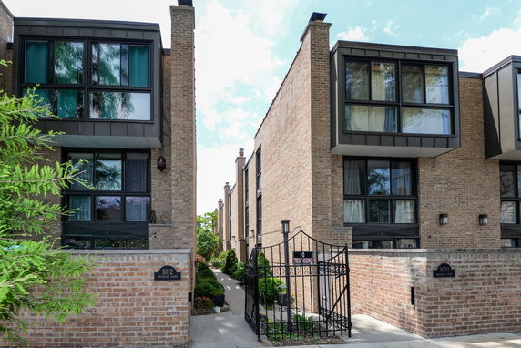 Front view of brick townhouses with large windows and gated entrance.