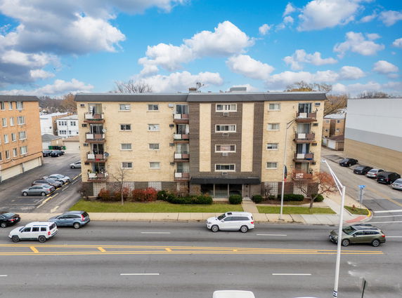 Front view of a four-story apartment building with balconies and parking area.