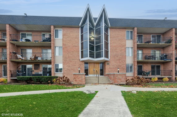 Front view of a multi-story brick apartment building with balconies and a prominent glass entrance.