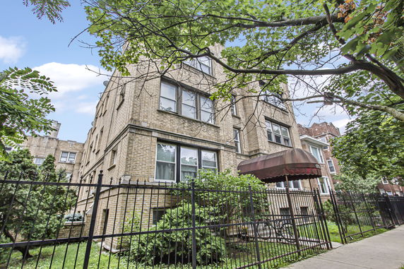Front view of a multi-story brick building with a metal fence and entrance canopy.